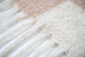 Dettaglio di sciarpa a maglia a quadri beige e bianchi con morbide frange ai bordi
