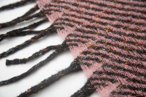 Dettaglio della sciarpa in maglia rosa e nera con spesse nappe e trama tweed maculata