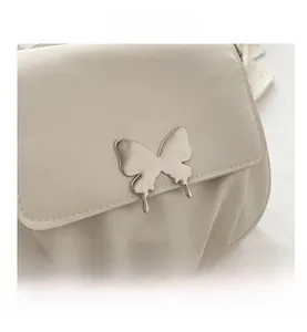 Detail of silver butterfly metal buckle and pleated leather on white crossbody bag