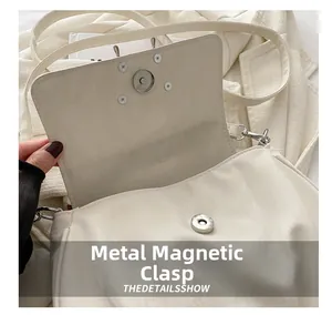 Detail view of the silver magnetic closure on a cream faux leather shoulder bag