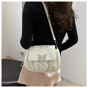 Detailed view of cream leather crossbody bag with silver butterfly buckle and pleats