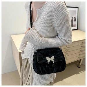Detail of glossy wrinkled texture and silver butterfly buckle on black shoulder bag