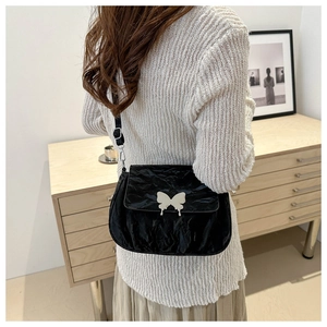 Detailed view of black pleated shoulder bag with a silver butterfly metal buckle worn by model