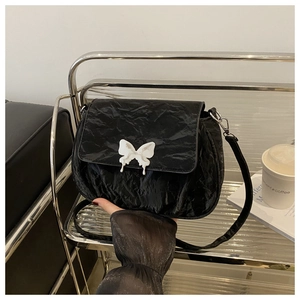 Detail of black pleated leather crossbody bag featuring a white butterfly metal clasp