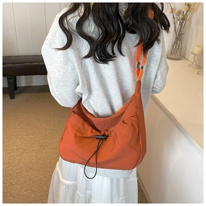 Detail of burnt orange nylon crossbody bag with drawstring ruched design and wide strap