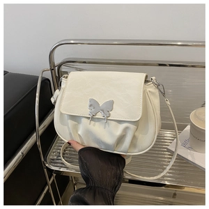 Macro detail of creamy white saddle bag featuring elegant pleats and silver butterfly buckle