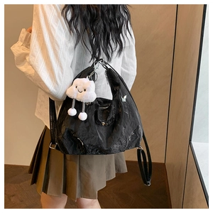 Detail of black pleated shoulder bag with silver butterfly charm and plush cloud pendant