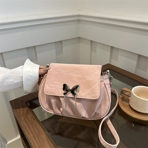 Pink ruched shoulder bag with butterfly metal clasp held against a cafe background