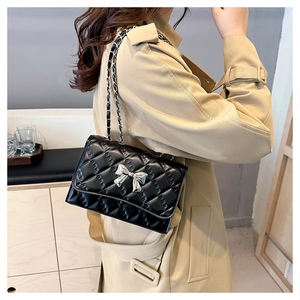 Detail of black quilted crossbody bag featuring a silver bow buckle and chain strap