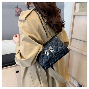 Close-up of black quilted shoulder bag with silver bow detail and metal chain strap