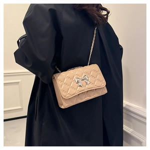 Detail of beige quilted crossbody bag featuring a silver bow accent and metal chain strap