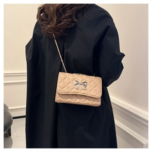 Detail of beige quilted chain shoulder bag featuring a silver bow metal buckle on premium leather