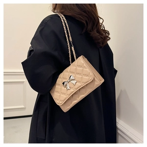 Detail of beige quilted chain bag featuring a silver metal bow buckle and elegant texture