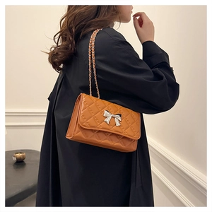 Detail of orange quilted crossbody bag with silver bow accent and chain shoulder strap