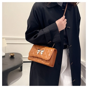 Detail view of brown quilted crossbody bag with silver bow clasp and metal chain strap