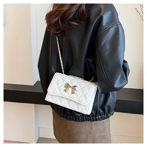 Detail of white quilted crossbody bag with golden bow clasp and chain strap on model