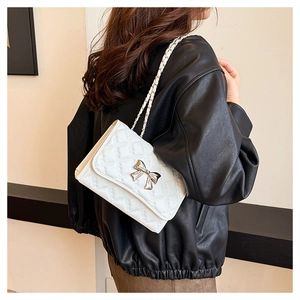 Detail of white quilted crossbody bag with silver metal bow and chain strap on model