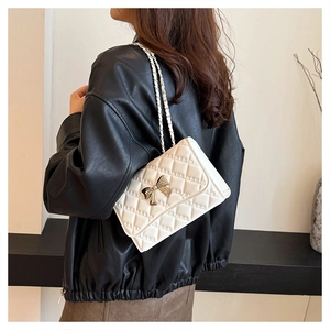 Detailed close-up of a white quilted crossbody bag with a gold bow buckle on a model