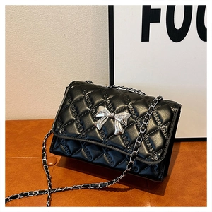 Close-up of quilted black leather bag featuring a silver metal bow buckle and chain strap