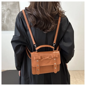 Rear view of a model wearing a brown leather backpack with heart embossing and bow details