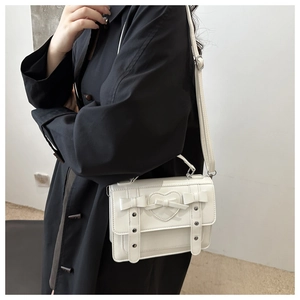 Detail of white PU messenger bag with heart patch and bow detail on a black coat
