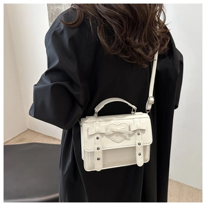 Detail of a white mini crossbody bag with a heart bow and silver studs on a black outfit