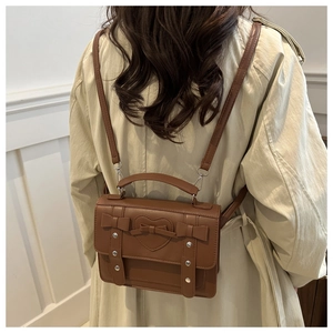 Brown PU leather backpack with heart embossing and bows shown on a beige trench coat