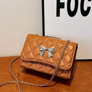 Brown quilted shoulder bag with silver bow accent and chain strap on a leather surface