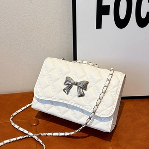 White quilted crossbody bag with silver bow accent and classic chain strap in minimalist setting