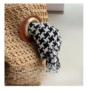 Detail of woven straw bag with gold eyelet and houndstooth pattern knot shoulder strap