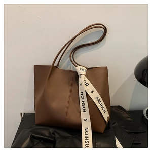 Detail of a brown leather tote bag featuring a decorative silk scarf on the handle