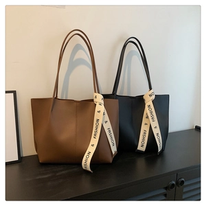 Detail of coffee and black leather tote bags featuring decorative printed ribbon handles
