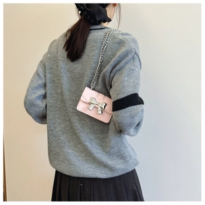 Pink mini crossbody bag with silver bow buckle and chain strap on a model's shoulder