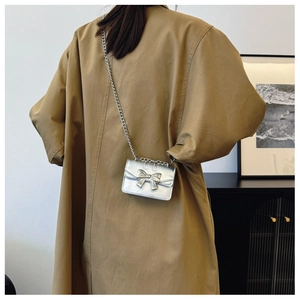 Silver mini chain bag with bow detail shown on a model wearing a brown trench coat