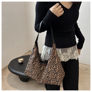 Leopard print canvas tote bag with black faux leather strap shown on model shoulder