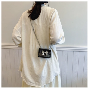 Mini sac bandoulière en cuir noir avec nœud argenté et chaîne porté par un modèle