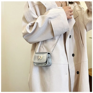 Détail du mini sac selle argenté avec ornement papillon porté sur un trench-coat chic