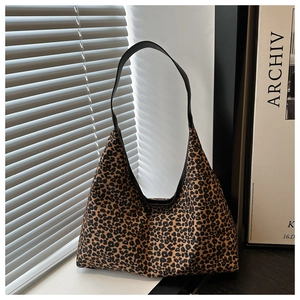 Detailed close-up of leopard print hobo bag with black leather strap on a textured background