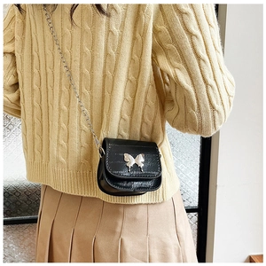 Mini black crossbody bag with silver butterfly buckle shown on a yellow sweater