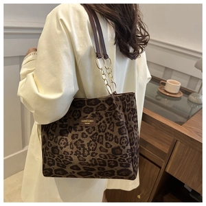 Leopard print tote bag with brown leather straps and gold metal rings shown on a shoulder