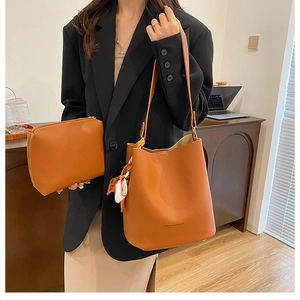 Orange-brown large leather bucket bag set with silk scarf and matching pouch on a desk