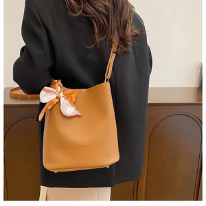 Detail of brown leather bucket bag with decorative scarf and protective metal bottom studs