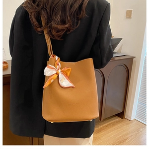 Detail view of brown pebbled leather bucket bag with fashion logo and silk scarf knot