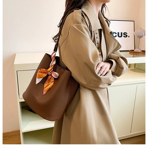 Detail of a large brown leather bucket bag with fashion print scarf on the handle