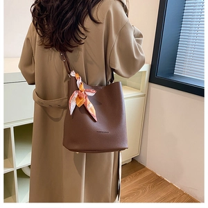 Detail of dark brown leather bucket bag with printed silk scarf on trench coat
