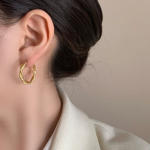 Elegant gold twisted hoop earrings with matte finish shown on model in close-up shot