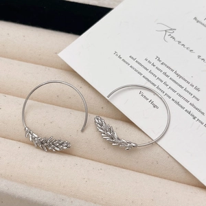 Macro detail of silver C-shaped hoop earrings with intricate wheat leaf relief engraving
