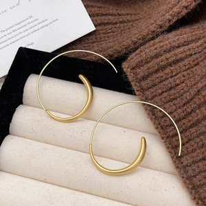 Minimalist matte gold spiral C-shaped hoop earrings on a warm aesthetic background