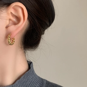 Minimalist twisted rope hoop earrings in gold finish worn by a model in soft lighting