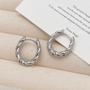Macro detail of silver twisted rope hoop earrings with polished texture on linen fabric